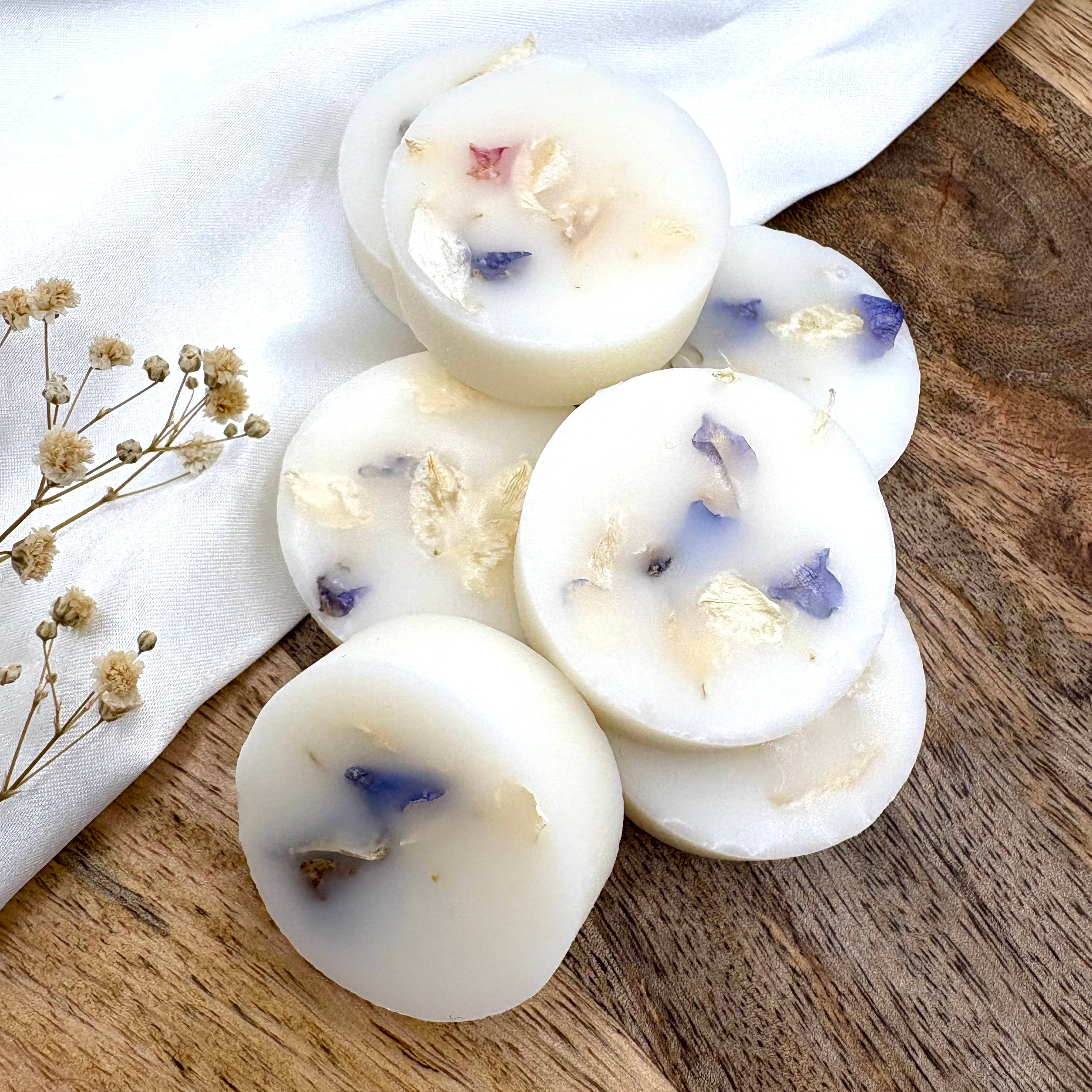 White wax melts with floral bits on a wooden surface with a white cloth and dried flowers.