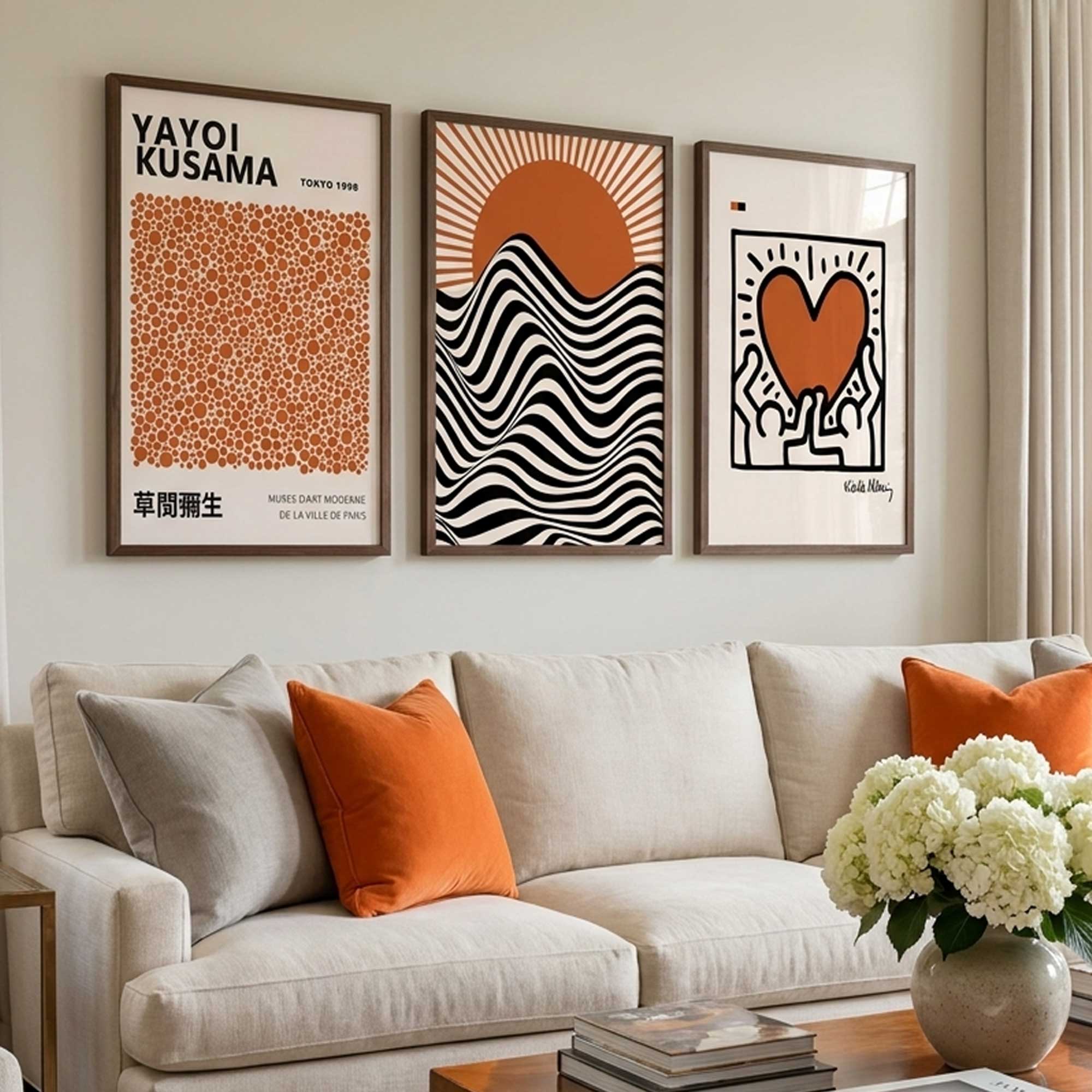 Living room with framed Keith Haring, Bauhaus and Yayoi Kusama artworks on the wall and a beige sofa with orange and grey pillows.