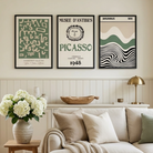 Three framed art prints featuring Picasso-themed designs hang on a cream wall above a beige sofa in a bright, modern living room. The prints have green, black, and white abstract and wavy patterns.