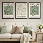 Three framed Matisse-style wall art prints hang above a cream sofa in a styled living room. The prints feature muted sage green and black line-art designs with text including 'MATISSE' and 'WILLIAM MORRIS.