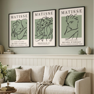 Three framed Matisse art prints with minimalist line art in sage green and black are displayed on a sage green wall above a beige sofa in a styled living room.