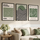 Three framed japandi art prints with green, black, and cream designs are displayed on a beige wall above a cream sofa in a styled living room setting.