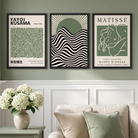 Three framed art prints featuring Yayoi Kusama and Matisse designs in a styled living room setting with a beige sofa, side table, and white flowers.
