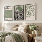 Three framed art prints with green, black, and white designs hang on a beige wall above a neatly made bed in a bright, modern bedroom.