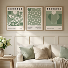 Three framed Bauhaus-style art prints in sage green and cream tones are displayed on a beige wall above a cream sofa with green and beige pillows in a bright, modern living room.