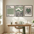 Three framed art prints with Japanese typography and abstract designs are displayed on a beige wall above a light wood desk and chair in a bright, modern room.