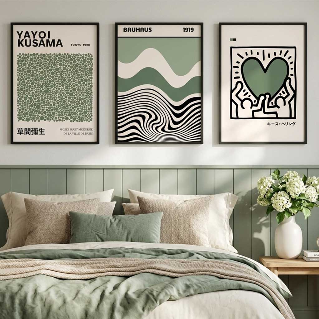 Three framed wall art prints with black frames hang above a bed in a styled bedroom. The prints feature abstract designs: a green patterned print reading 'YAYOI KUSAMA', a Bauhaus-style green, white, and black wavy pattern print, and a black-and-green heart artwork.