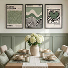 Three framed art prints with Japanese text and abstract designs are displayed on a wall above a styled dining table with white flowers in a vase.
