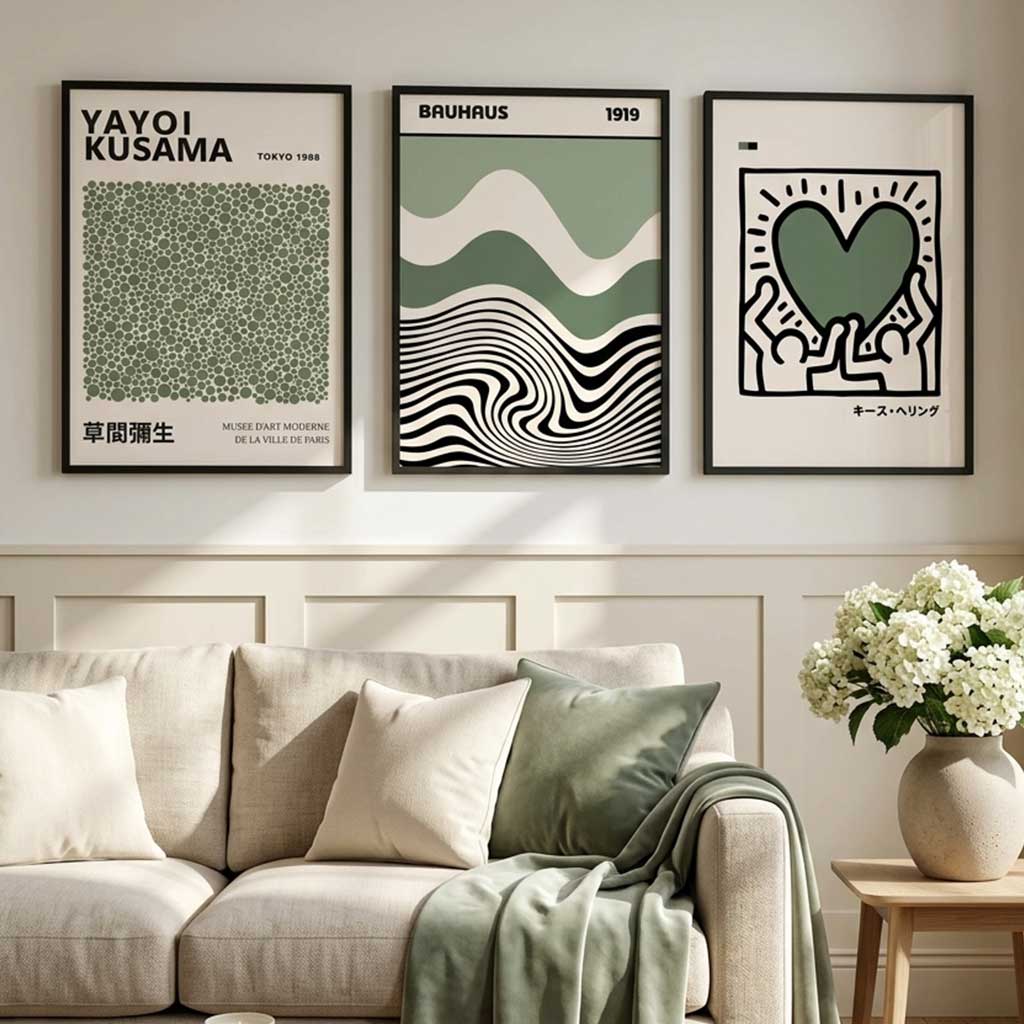 Three framed abstract art prints in a modern living room setting above a beige sofa with green and cream pillows and a throw blanket. The prints feature minimalist designs in green, black, and white, including a heart motif and wavy patterns.