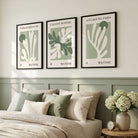 Three framed Matisse-inspired botanical art prints in black frames hang above a bed in a styled bedroom. The prints feature abstract coral or leaf-like shapes in muted green and off-white on pale sage backgrounds, with French text at the top of each print.