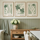 Three framed Matisse art prints with abstract coral-like designs in sage green and cream hang on a beige wall above a wooden console table in a styled dining/kitchen setting.